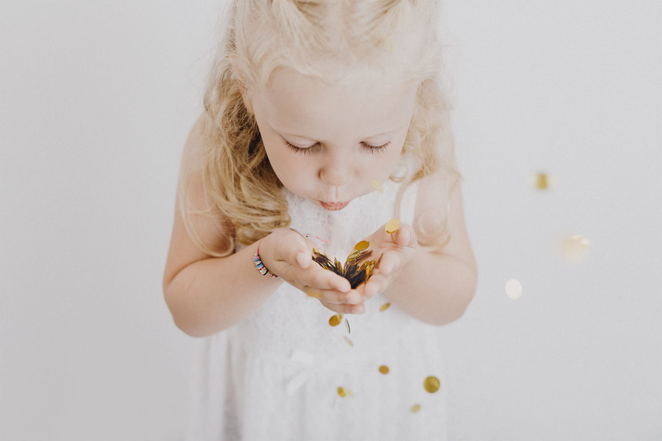 Ein blondes Mädchen mit Locken beim Kinder Fotoshooting, das Goldglitzer in die Luft pustet