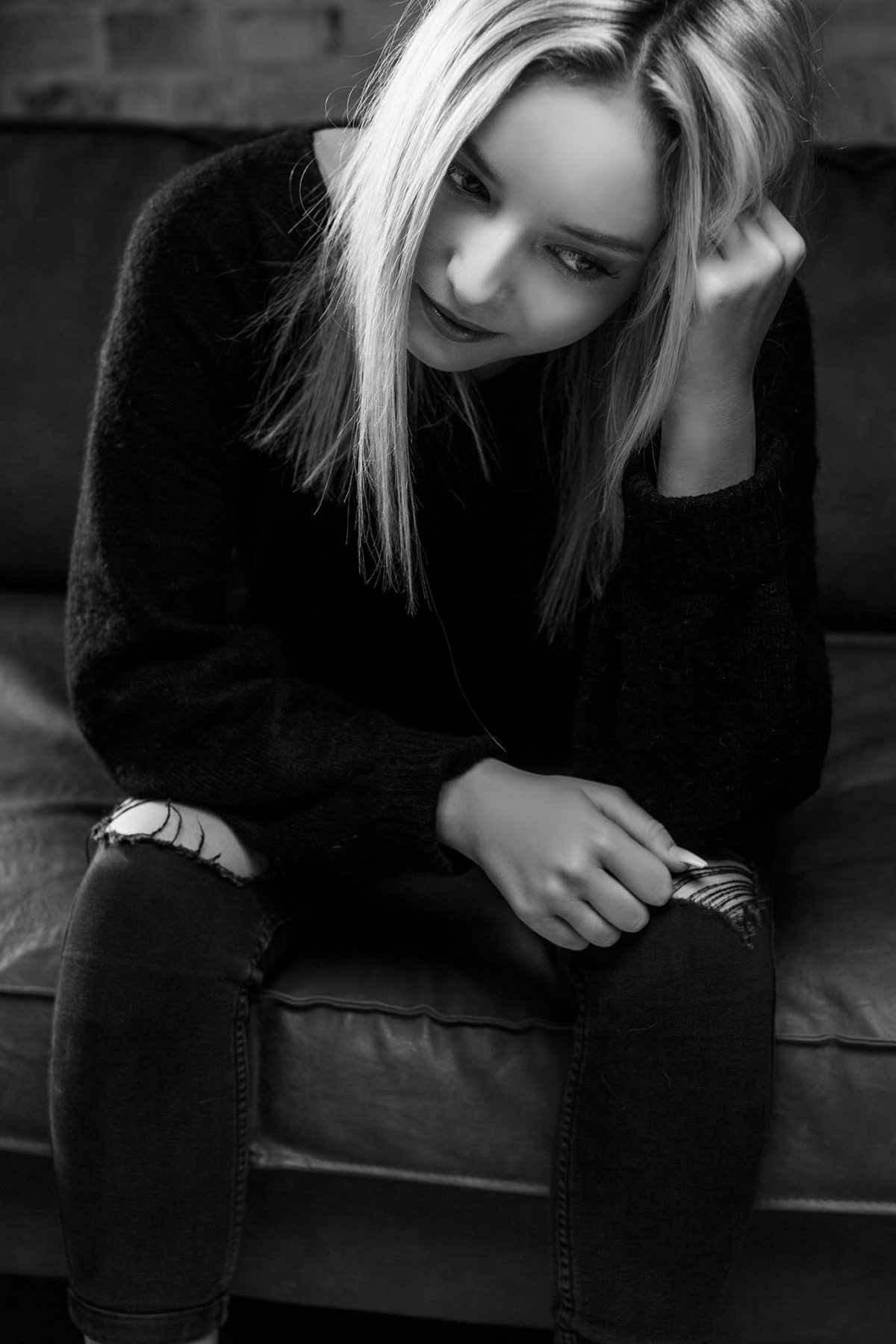 Schwarzweiss Fotografie einer blonden, jungen Dame in Schwarz gekleidet